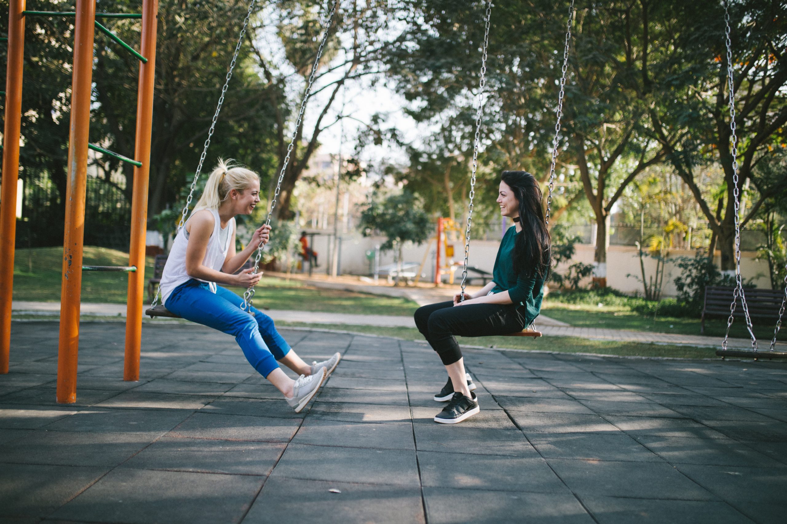 Two women laugh on the swings on a sunny day