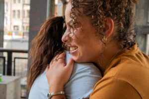 Side view of two women hugging, smiling